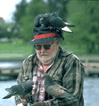 plaid-shirted, bearded, in shades, covered by pigeons at lake