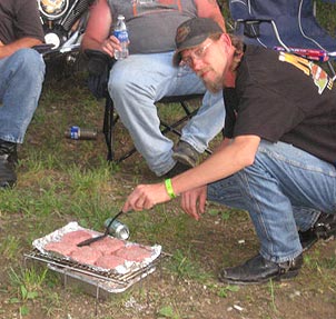 biker poses over raw burgers on makeshift grill